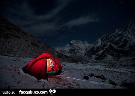 Tenda illuminata di notte in mezzo alle montagne innevate