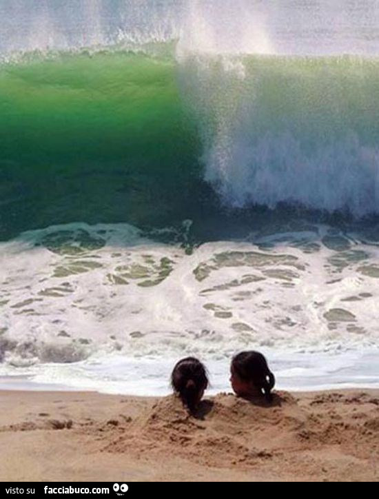 Bambine sotto la sabbia a riva mentre arriva onda altissima