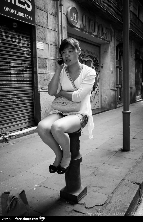Ragazza asiatica al telefono seduta sopra un paletto